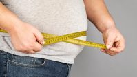 A man measures his fat belly with a measuring tape. on a gray ba