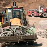 An excavator carries the damaged parts of the auger machine used for the drilling to rescue the trapped workers inside the Silkyara Tunnel