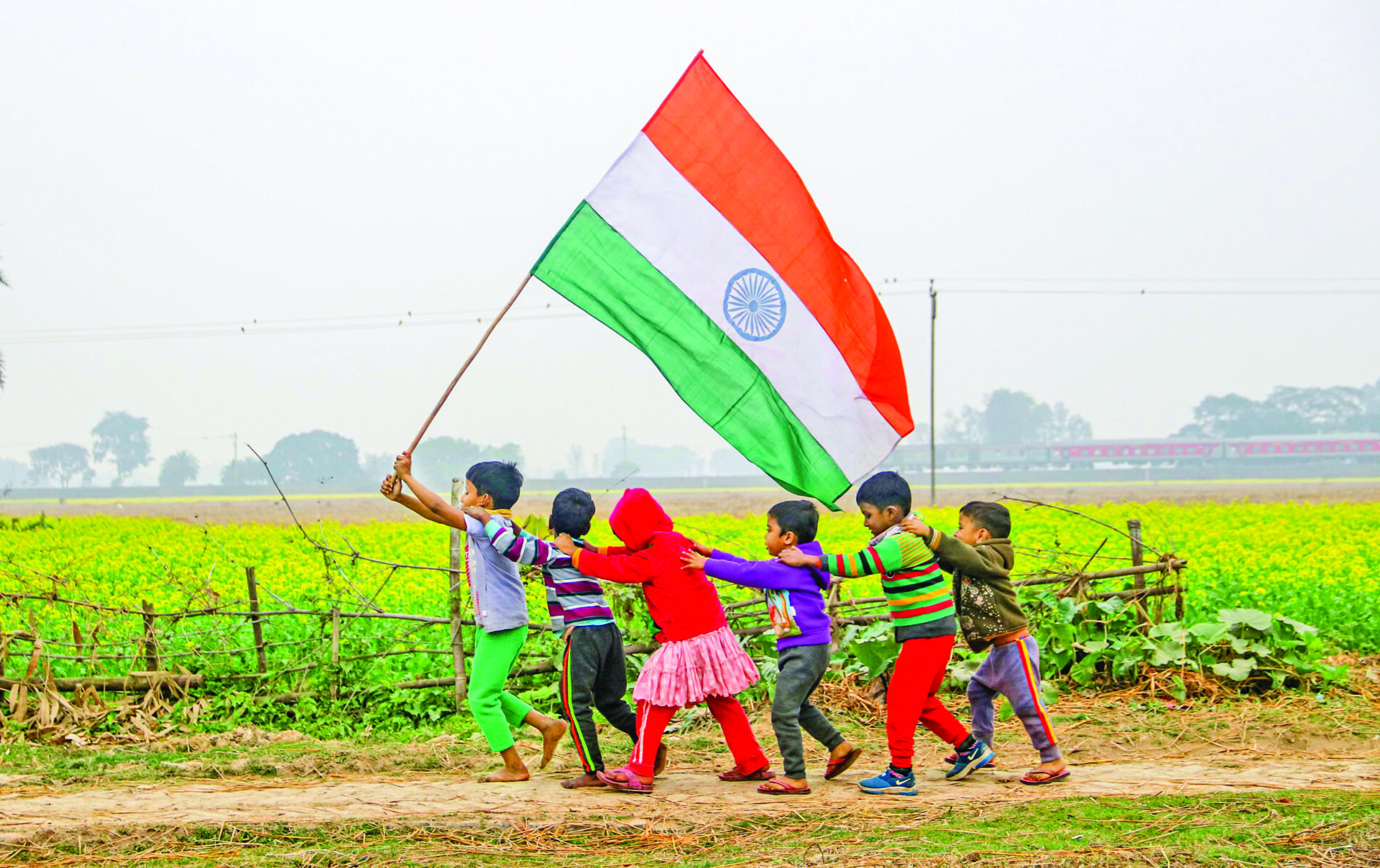 Children holding the National Flag run through a mustard field ahead of Republic Day celebrations, at a village near Balurghat in Bengal’s South Dinajpur on Saturday. ANI