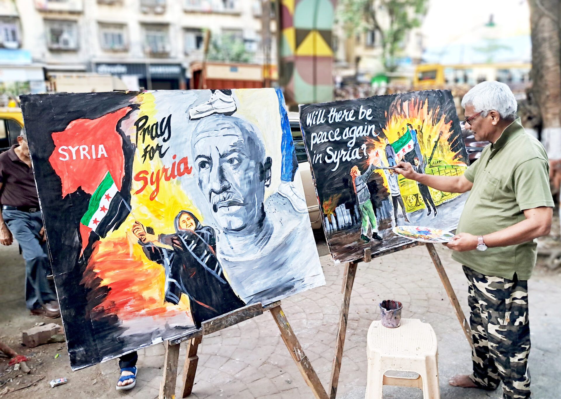 A Gurukul School of Art teacher makes paintings on the Syria issue, alongside a road, in Mumbai on 9 December. ANI