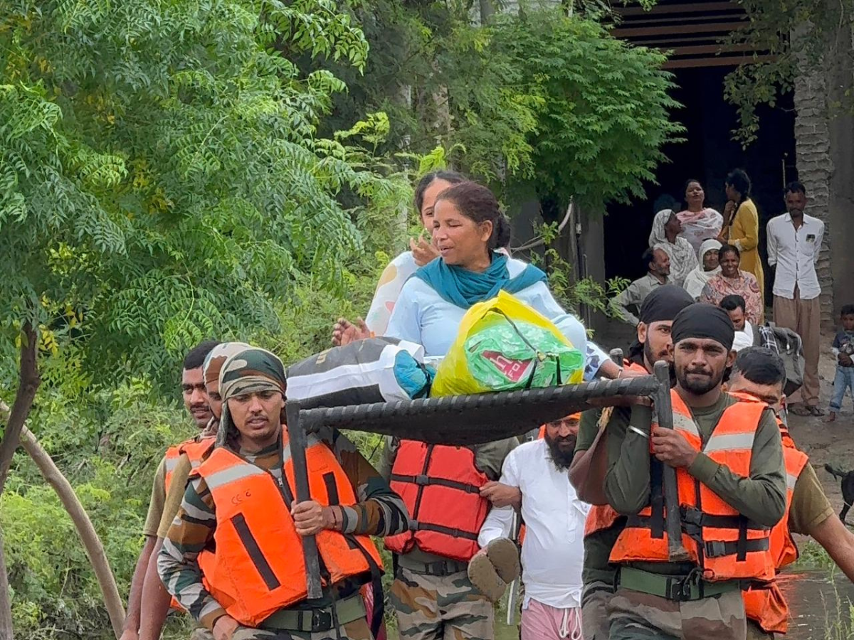Army personnel carry a bedridden cardiac patient on her bed through floodwaters